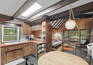 A rustic cabin interior with a kitchen, dining area, and a bed with a view. - Cozy 2-bedroom chalet cabin retreat in Pocono Lake. Ski, Gym, Campfire, Hiking (Pocono Lake)