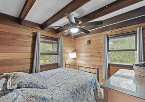 A wooden cabin bedroom with a bed, a ceiling fan, and a window.