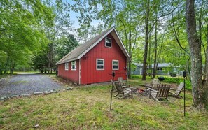 A red cabin with a gravel driveway, surrounded by trees, and a fire pit with chairs. - Cozy 2-bedroom chalet cabin retreat in Pocono Lake. Ski, Gym, Campfire, Hiking (Pocono Lake)