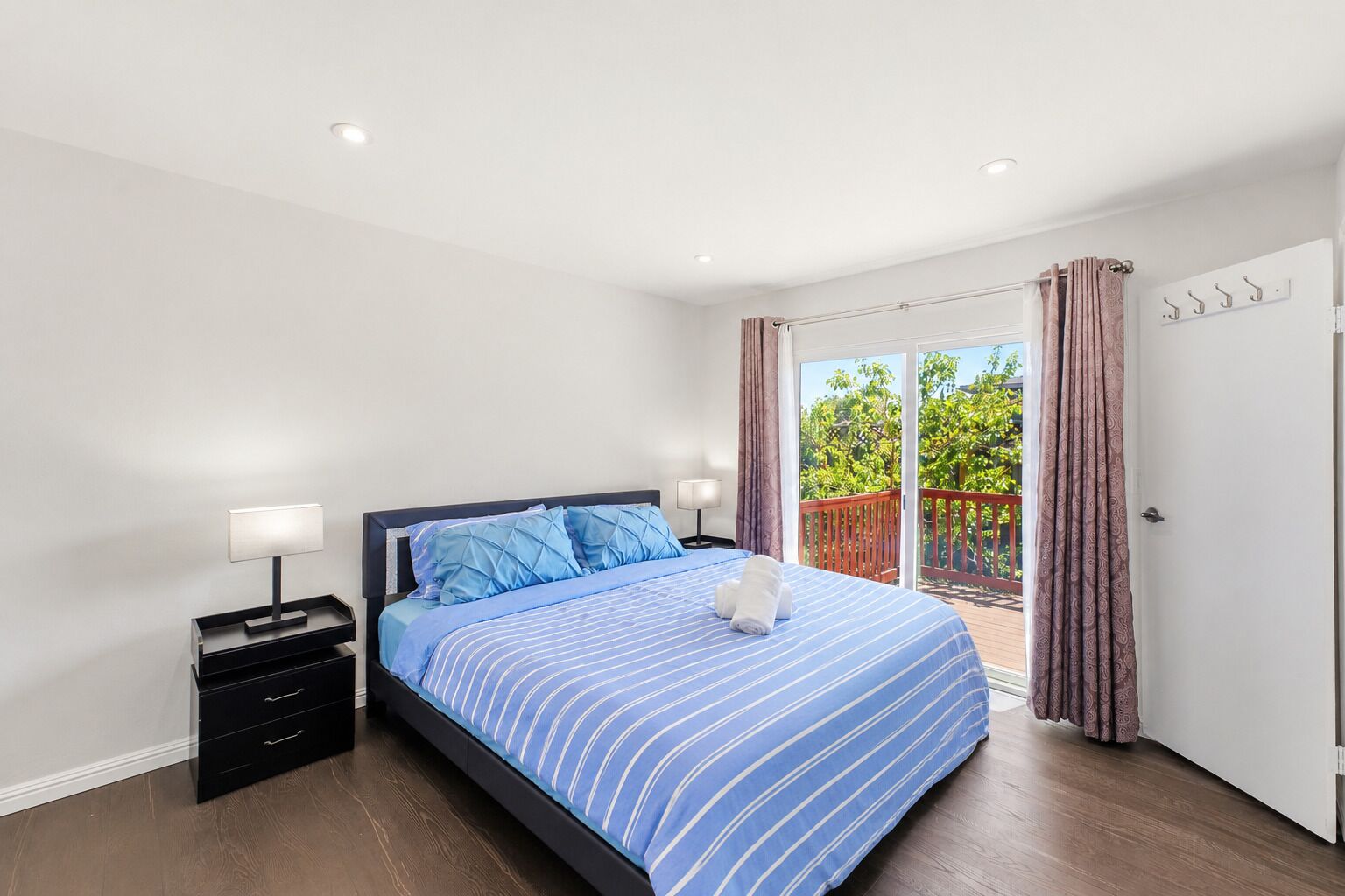 Une chambre à coucher comprenant un lit, des tables de chevet, une porte-fenêtre coulissante donnant sur un espace extérieur et une porte blanche.