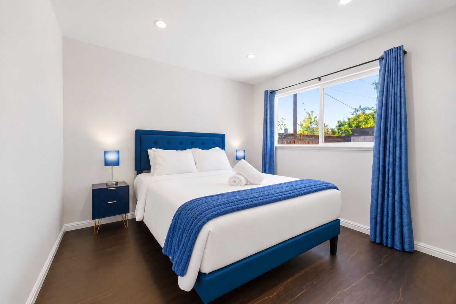 Une chambre moderne avec un grand lit, une table de chevet, une fenêtre avec des rideaux et une vue sur la verdure.