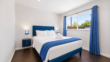 Une chambre moderne avec un grand lit, une table de chevet, une fenêtre avec des rideaux et une vue sur la verdure.