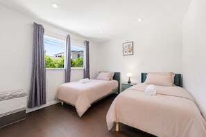 Een hotelkamer met twee bedden, een raam met gordijnen, een wandlamp en een klein schilderij.