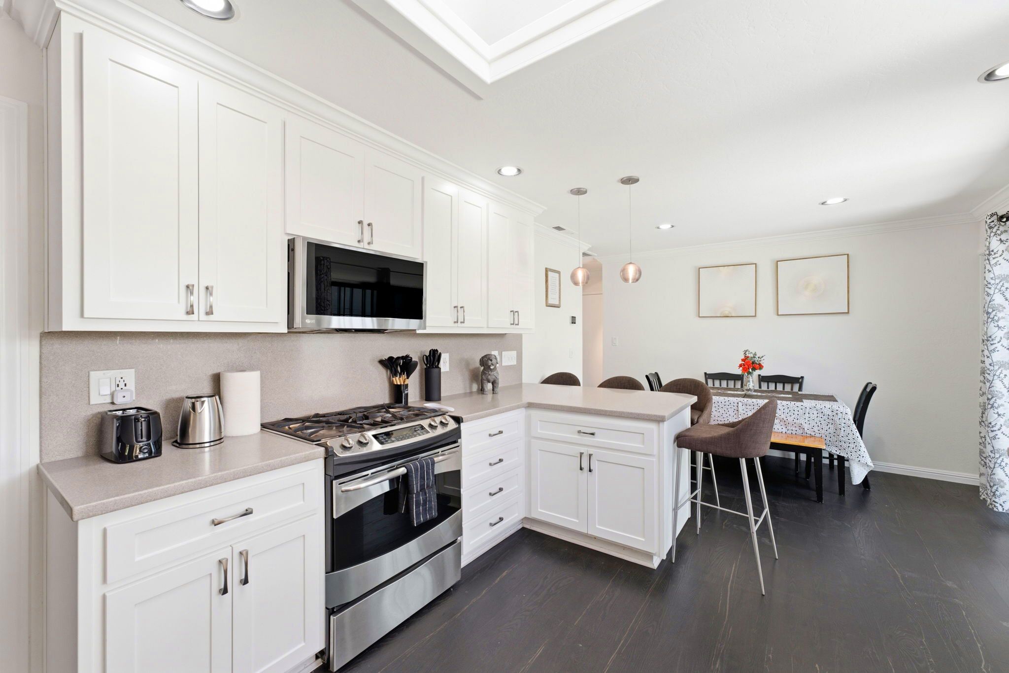 Une cuisine moderne avec des meubles blancs, une cuisinière en acier inoxydable et un coin repas comprenant une table et des chaises.