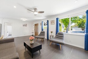 Una sala de estar moderna con piso de madera oscura, ventilador de techo y un ventanal con cortinas azules.