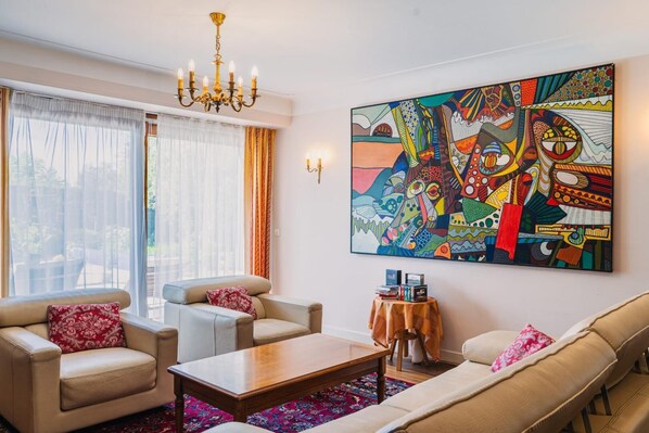A living room with a sofa, armchairs, a coffee table, a chandelier, and a colorful abstract painting. - L'Orée du Bois - SAUGNAC ET CAMBRAN (SAUGNAC ET CAMBRAN)
