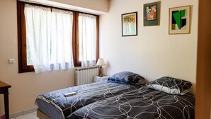 Ein Schlafzimmer mit zwei Betten, einem Heizkörper, einer Lampe und drei gerahmten Kunstwerken an der Wand.