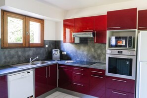 A kitchen with red cabinets, a built-in microwave, a dishwasher, and a water dispenser. - L'Orée du Bois - SAUGNAC ET CAMBRAN (SAUGNAC ET CAMBRAN)