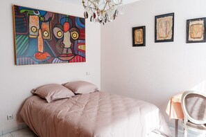 Ein Schlafzimmer mit einem Bett, einem Sessel, einer Chandelierleuchtre und drei gerahmten Kunstwerken an der Wand.