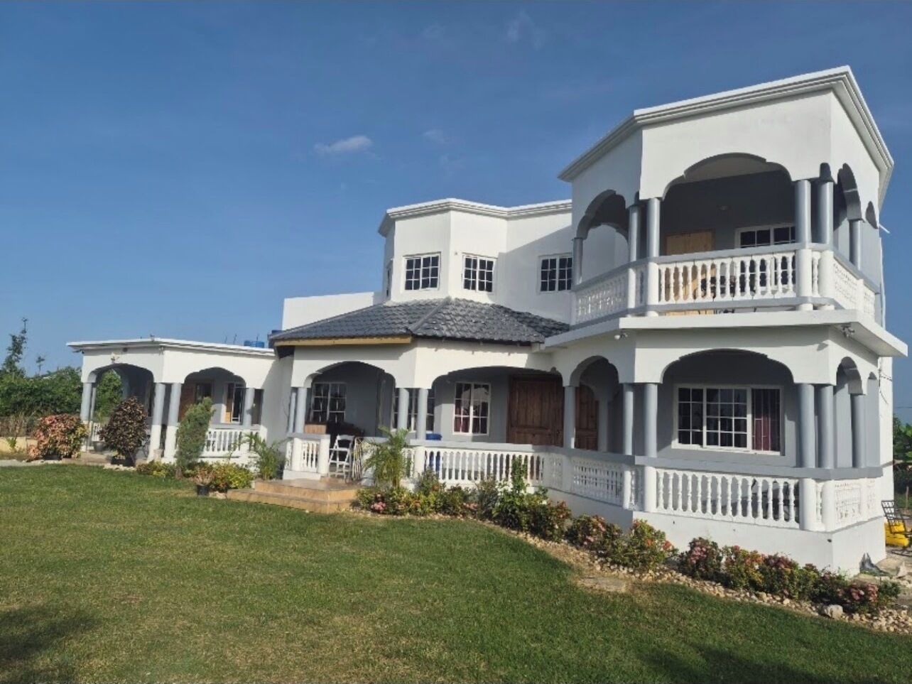 A large, two-story house with a white exterior, multiple balconies, and a well-maintained lawn.