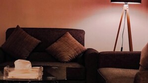 Una habitación con un sofá, una mesita con lámpara y un televisor montado en la pared.