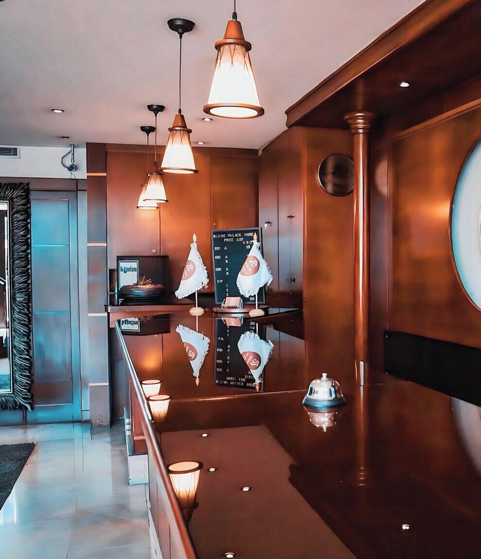 A hotel lobby with a reception desk, pendant lighting, and a large mirror.