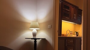 Una habitación con una lámpara de mesa, una silla y vistas hacia una zona de cocina con armarios y una encimera.