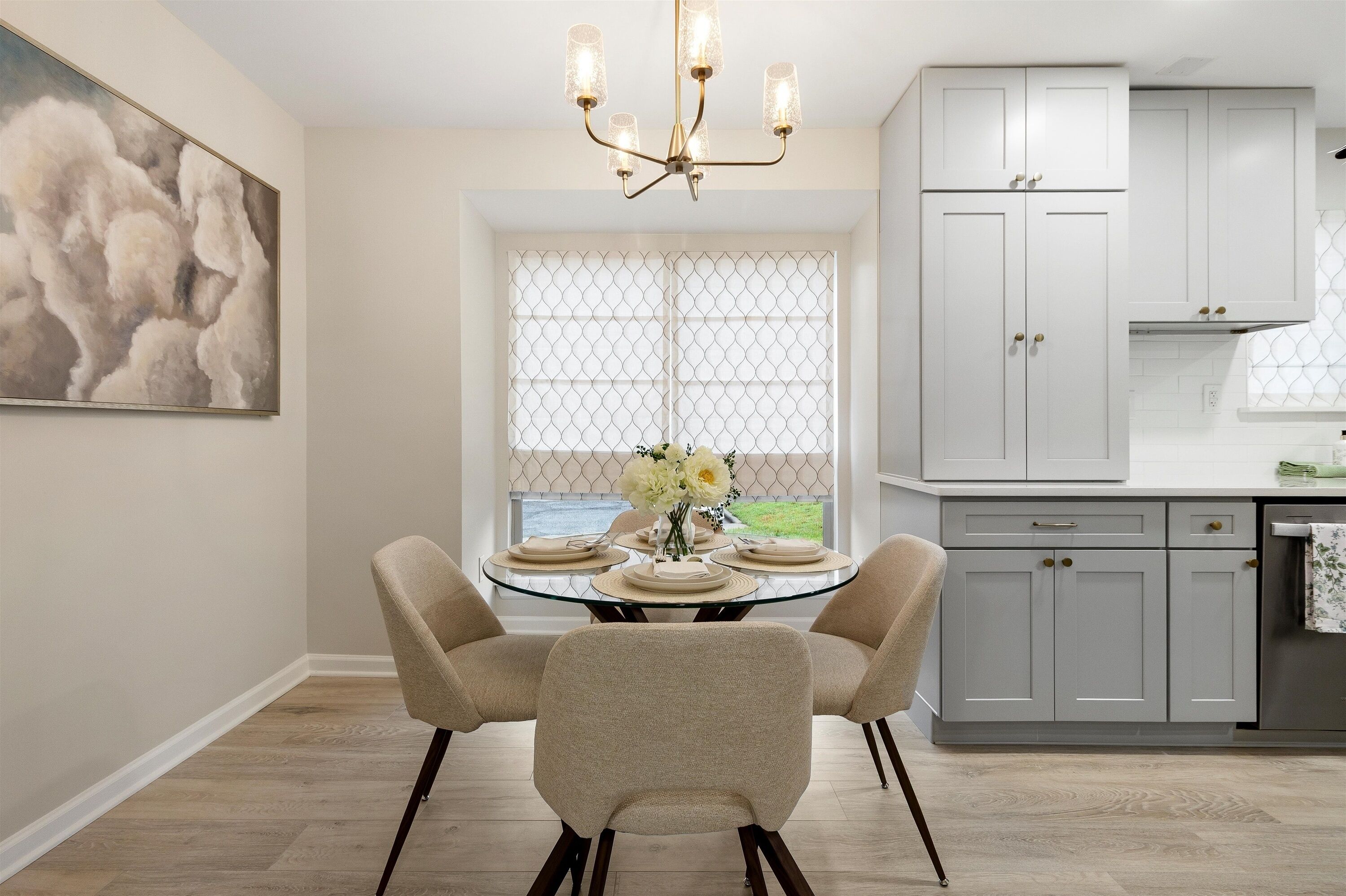 A dining area with a glass table, two chairs, a chandelier, and a window with a view.