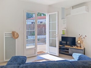 A living room with a sofa, a TV, a sliding glass door, and a small table with a vase. - Les Cariatides 8 by Interhome (Ile d'Oléron)
