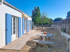 A building with blue doors, a wooden deck, and a table with fruit. - Les Cariatides 8 by Interhome (Ile d'Oléron)