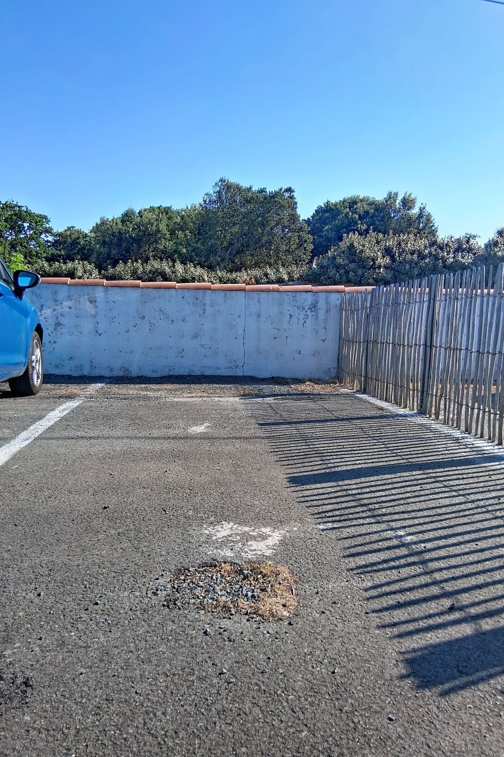 A parking area with a blue car, a concrete wall, and a wooden fence.