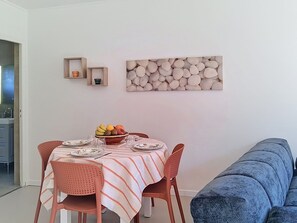 A dining area with a table set for two, a bowl of fruit, and a wall-mounted art piece. - Les Cariatides 8 by Interhome (Ile d'Oléron)