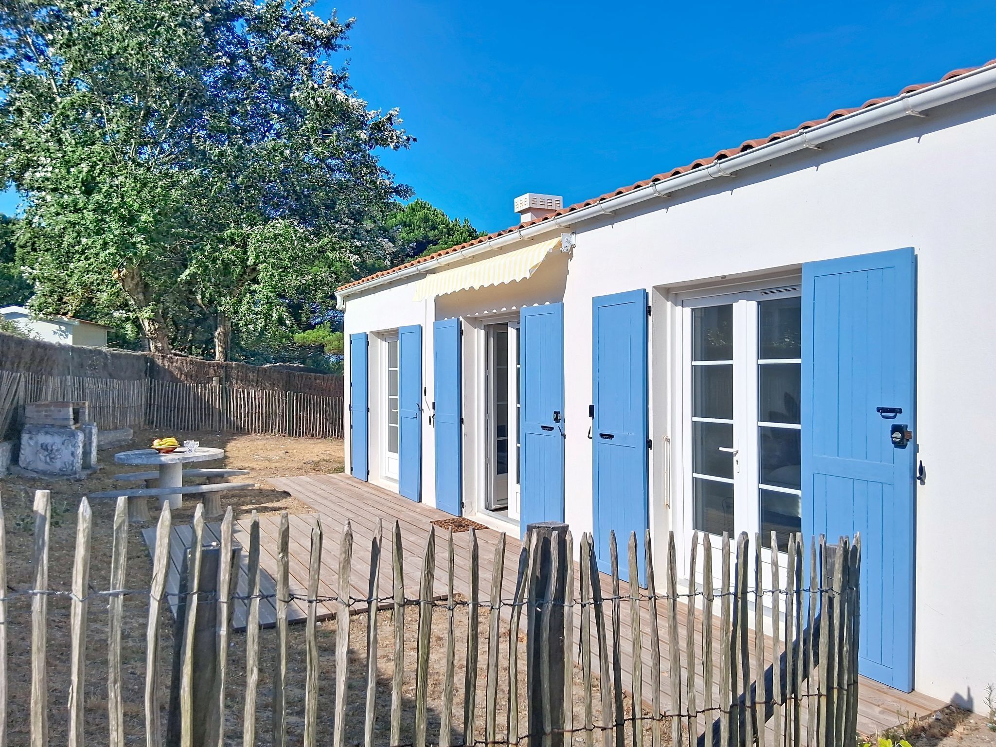 A white building with blue shutters, a wooden deck, and a fenced yard.