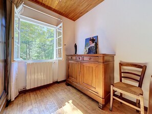 A room with a wooden floor, a radiator, a window with curtains, a wooden cabinet, and a chair. - La Bergerie de Portes by Interhome (Portes)