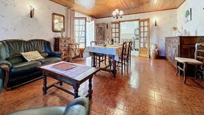Ein gemütliches Wohnzimmer mit Holzboden, einem grünen Sofa, einem Esstisch mit Stühlen und einem durchgehenden Durchgang zur Küche.