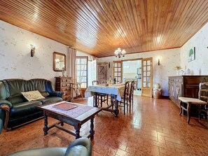 A cozy living room with a wooden ceiling, a green sofa, a dining table with chairs, and a kitchen area visible through an open door. - La Bergerie de Portes by Interhome (Portes)