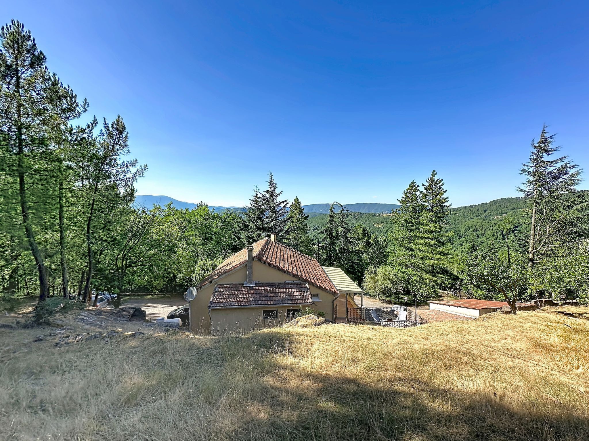 Una baita rustica con tetto in tegole, circondata da una foresta e colline sullo sfondo.