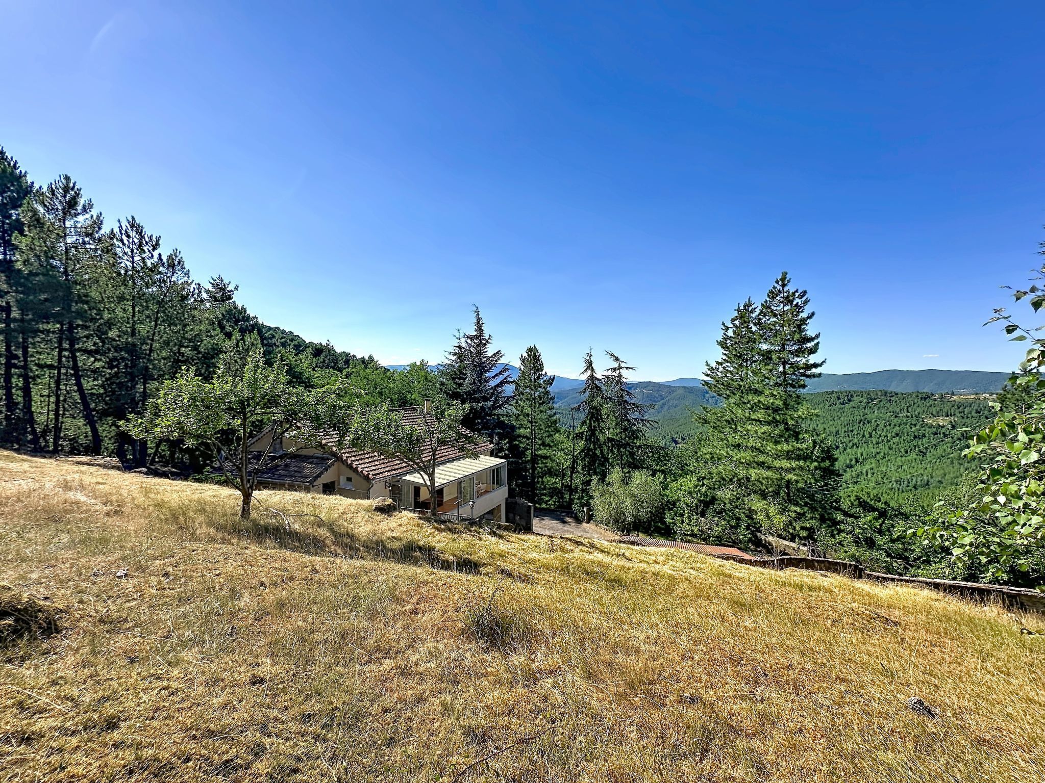 A house with a sloped roof, surrounded by trees and a view of distant mountains.