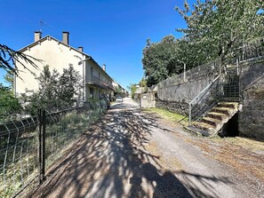 Un carrer estret flanquejat per edificis, una tanca i una paret de pedra.