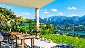 A patio with a table, chairs, and a lounge chair overlooking a mountainous landscape. - Karawanken Panorama by Interhome (Ludmannsdorf)