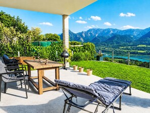Eine Terrasse mit Tisch, Stühlen und einer Liege mit Blick auf eine gebirgige Landschaft.
