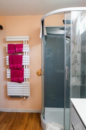 Un baño con cabina de ducha de vidrio, un perchero con toallas rosas y un radiador blanco.