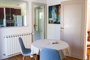 Ein Zimmer mit Esstisch, zwei Stühlen, Heizkörper, Tür und einem Bild an der Wand.