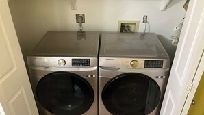 Un espace buanderie équipé de deux machines à laver Samsung, d’une prise de courant et d’un petit cadre photo accroché au mur.