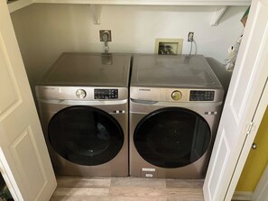 A laundry area with two Samsung washing machines, a power outlet, and a small picture frame on the wall. - Private Room with Attached Half Bath in Quiet Sherwood Home (sherwood)