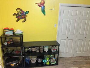 A kitchen with a black shelf unit holding plates, bowls, and kitchenware. A white door is visible in the background. - Private Room with Attached Half Bath in Quiet Sherwood Home (sherwood)
