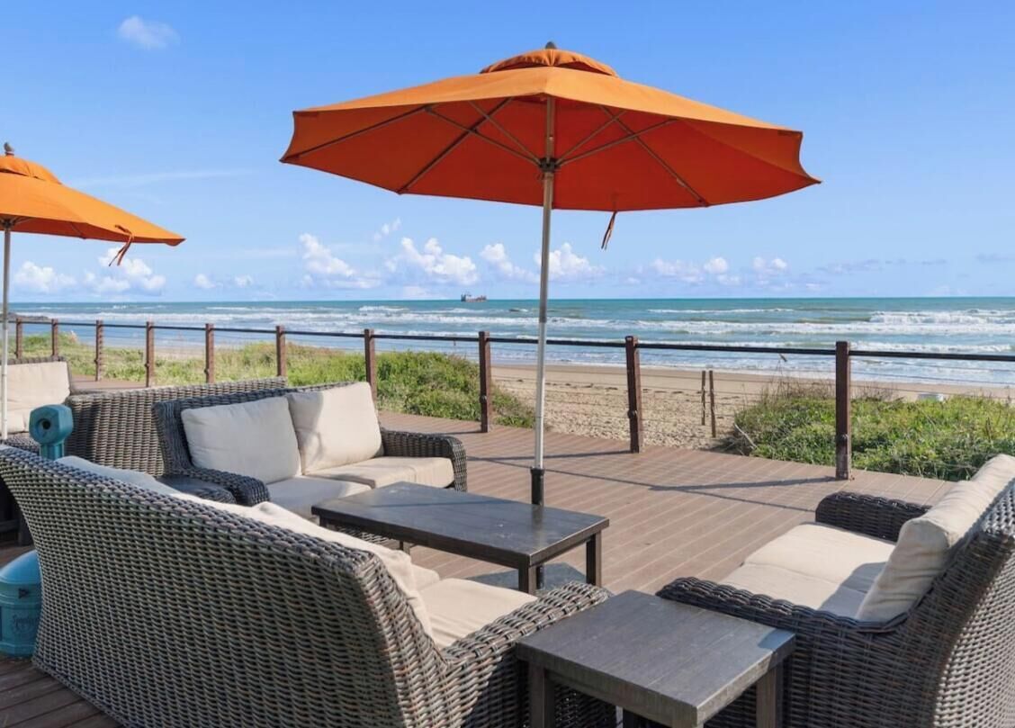 Un patio frente a la playa con mobiliario de mimbre y sombrillas naranjas.