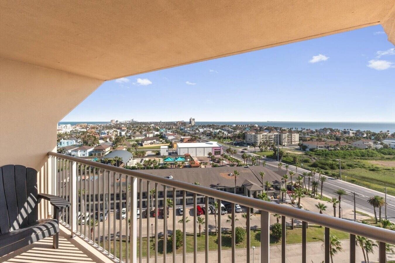Een balkon met uitzicht op een kustplaats, inclusief gebouwen, wegen en een heldere lucht.
