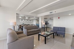 Un grand espace de vie comprenant un canapé, un fauteuil et une table basse, un coin repas avec des chaises et une table, et une cuisine à l’arrière-plan.