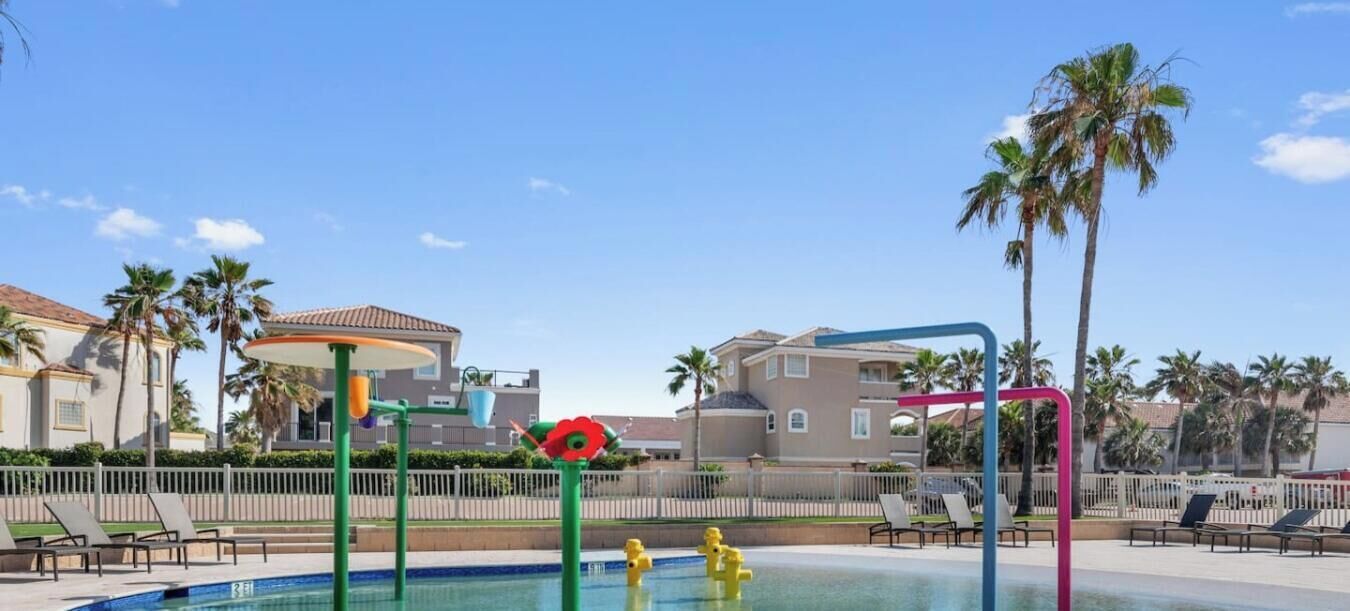 A swimming pool with lounge chairs, palm trees, and a building with a tiled roof.