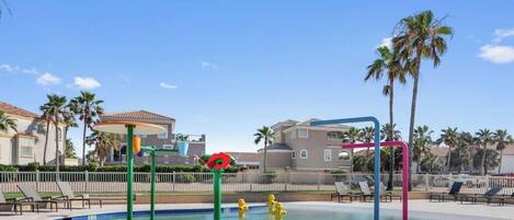 A swimming pool with lounge chairs, palm trees, and a building with a tiled roof.
