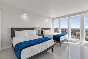 Une chambre d’hôtel moderne avec deux lits, une table de chevet et de grandes fenêtres donnant sur la ville.