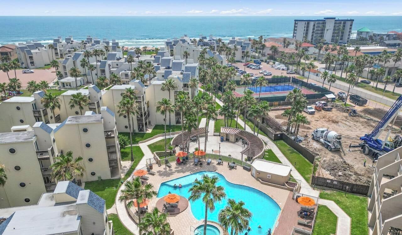 A resort with a swimming pool, palm trees, and a view of the ocean.