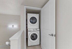 A laundry room with two stacked washing machines and a light fixture above. - 11th Floor Panoramic Views Sunset SpaceX Fireworks (South Padre Island)