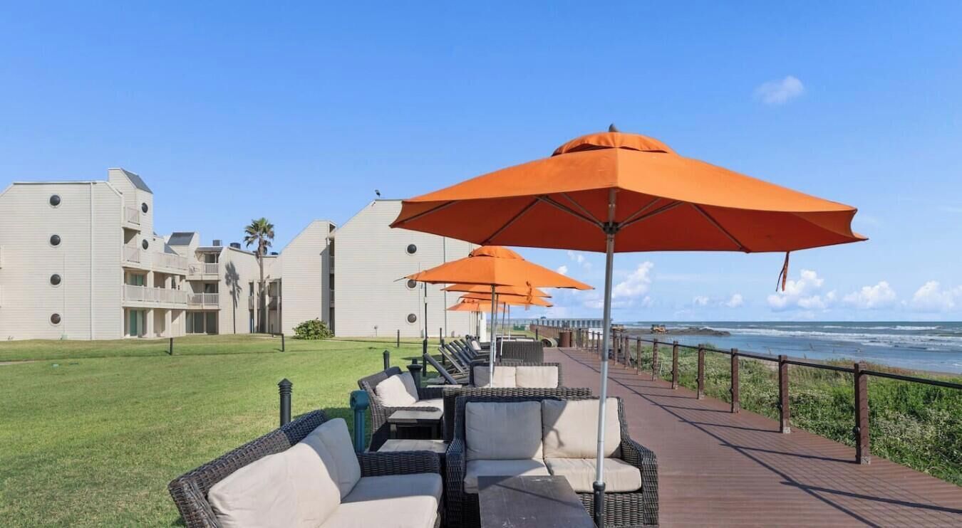 A seaside patio with outdoor seating and umbrellas, overlooking the ocean.