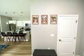 Een moderne keuken met witte kasten, een centraal eiland en barstoelen. Drie ingelijste foto's hangen aan de muur.