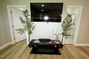 A room with a TV mounted on the wall, a black entertainment unit with chess pieces, and two potted plants. - Orlando Escape • Near Disney • 5 Bedrooms (Orlando)