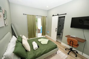 A bedroom with a bed, a desk, a TV, and a sliding door.