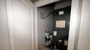 Un corridoio stretto con una porta in fondo, una presa elettrica a parete e un estintore.