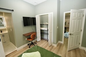 Een slaapkamer met een bed, een bureau, een stoel, een televisie, een kast en een deur naar een andere kamer.